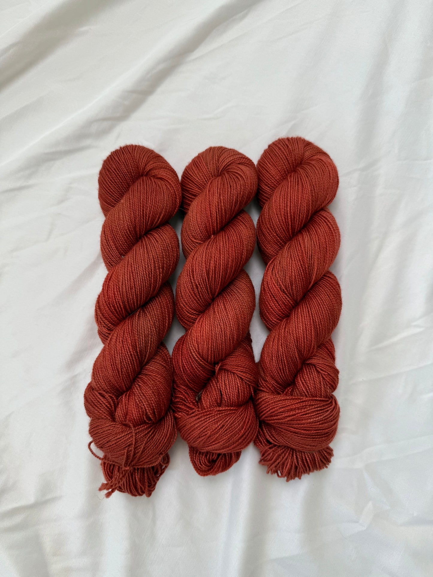 Three skeins of rust-colored yarn on a white fabric background