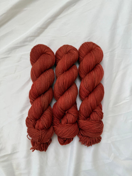 Three skeins of rust-colored yarn on a white fabric background