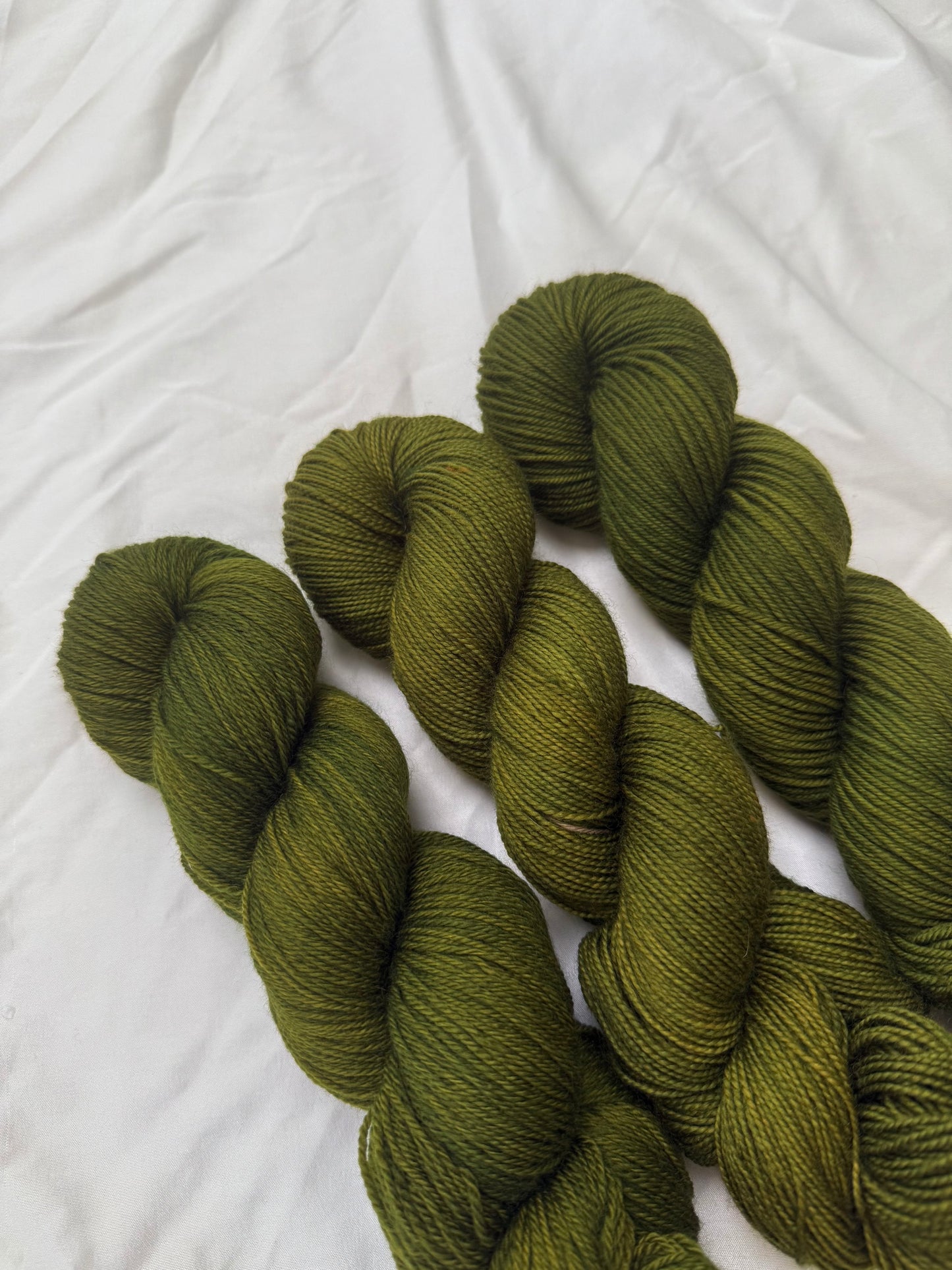 Three skeins of green yarn on a white textured fabric background