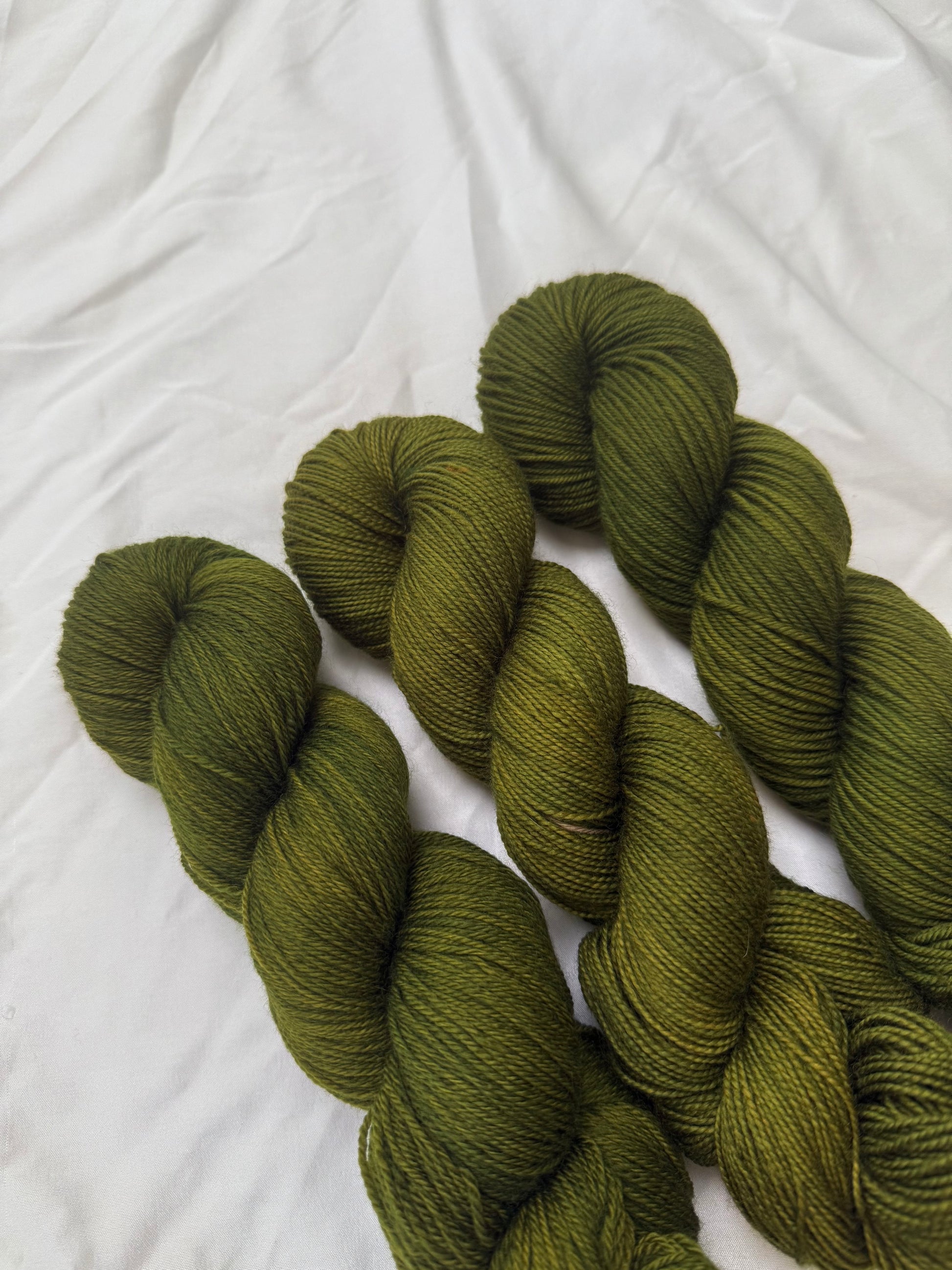 Three skeins of green yarn on a white textured fabric background