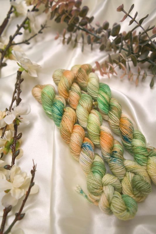 custom variegated hand dyed yarn with cream, butter yellow, creamsicle orange and grass green with teal speckles on nylon superwash sock weight