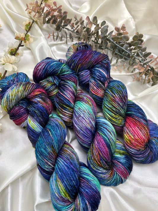 custom variegated hand dyed yarn with midnight blue, violet, teal and deep pink with yellow and green speckles on superwash merino yarn dk weight