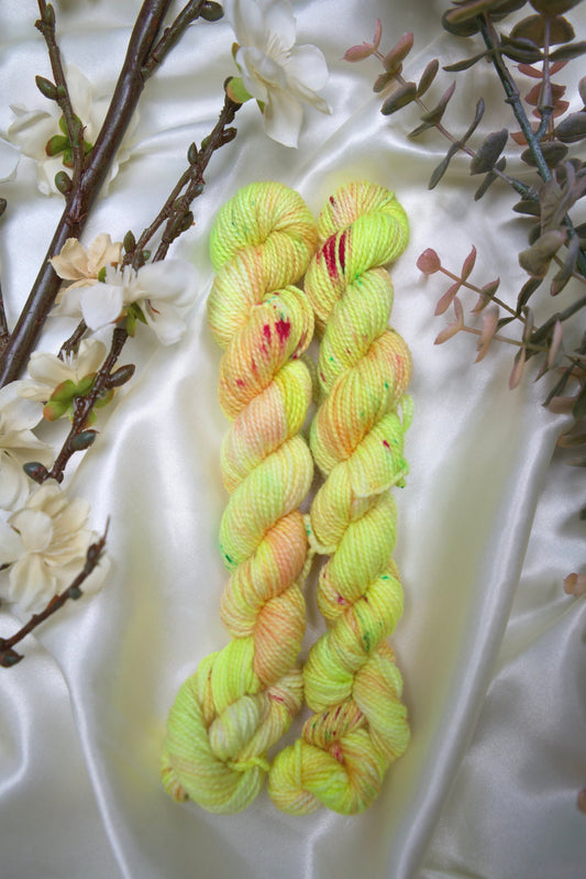 custom variegated hand dyed yarn with neon yellow and pastel peach with cherry red and green speckles on nylon superwash sock yarn