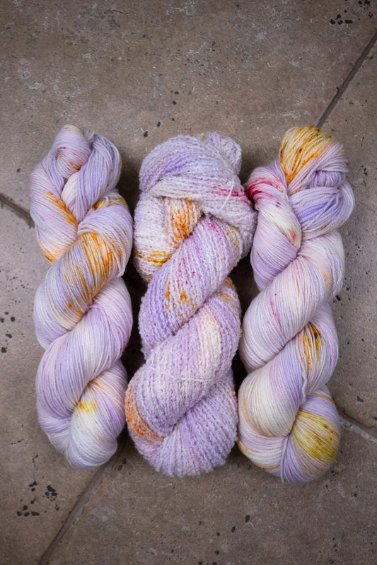 custom variegated hand dyed yarn with pastel lilac and soft purple with gold, orange and cherry red speckles on superwash merino yarn fingering weight