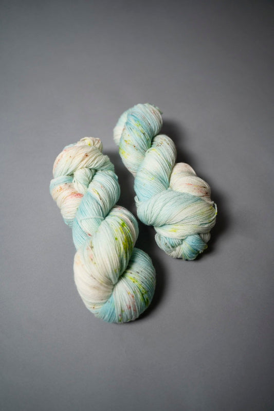 custom aqua, sky blue, teal variegated hand dyed yarn with neon green and salmon pink speckles on superwash merino fingering weight