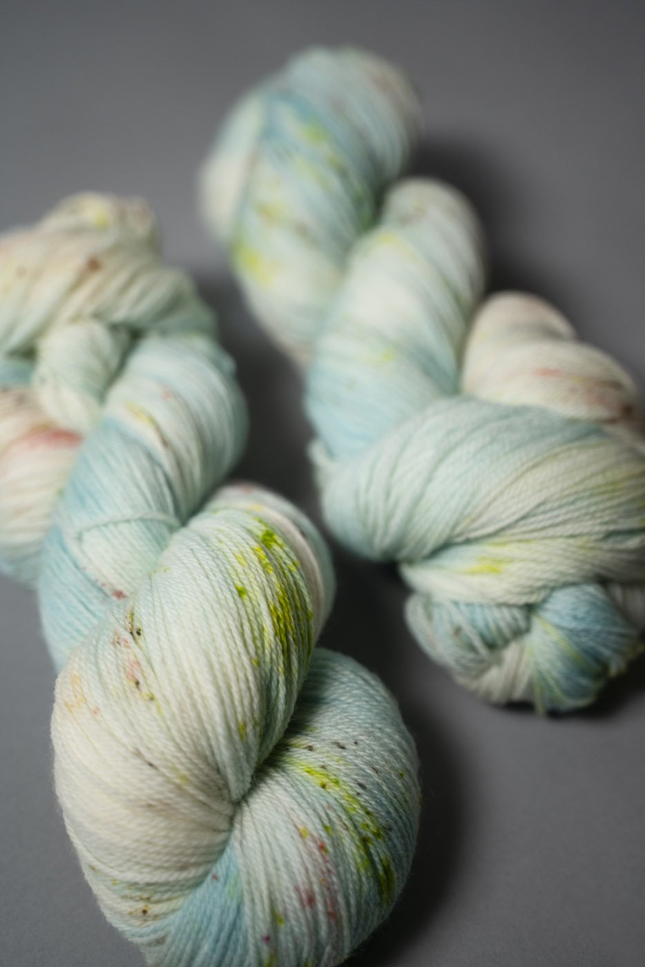 custom aqua, sky blue, teal variegated hand dyed yarn with neon green and salmon pink speckles on superwash merino fingering weight