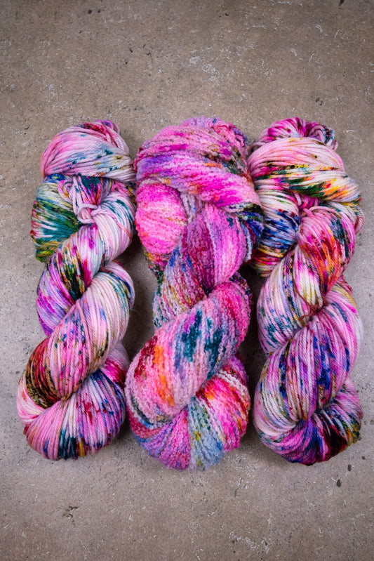 custom variegated hand dyed yarn with blue, neon pink, lichen, magenta, cherry red and yellow speckles on superwash merino worsted weight and boucle yarn