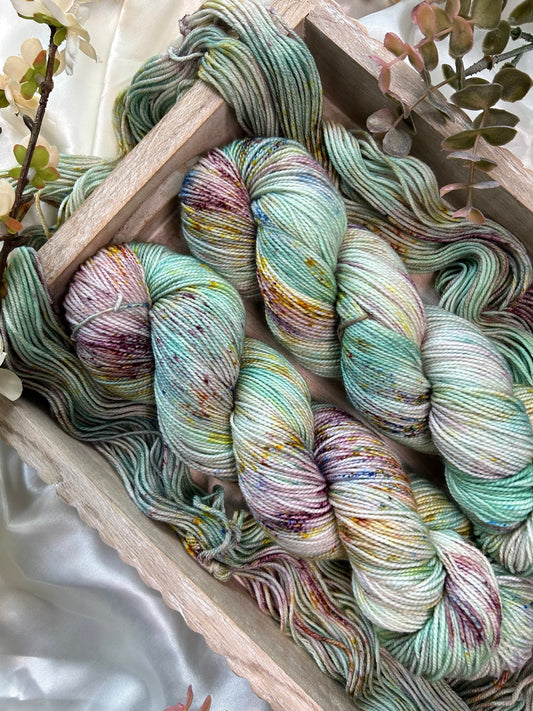 custom aqua, light teal, mint green, cream variegated hand dyed yarn with burgundy, gold, and indigo blue speckles on superwash nylon sport weight