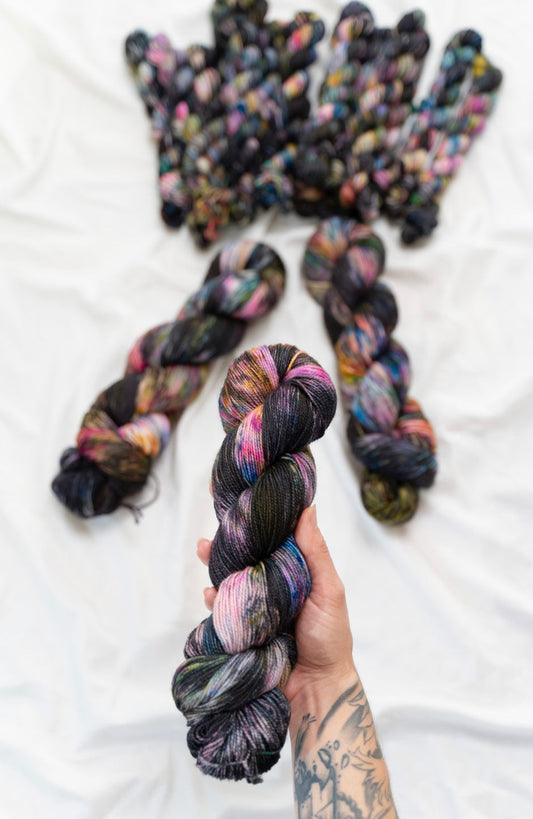 Hand holding multicolored yarn skeins with more yarn skeins in the background on a white surface.