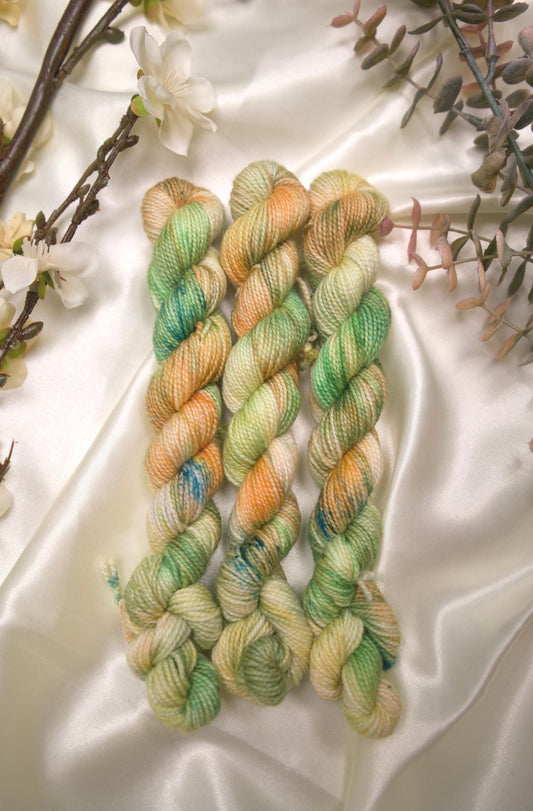 custom variegated hand dyed yarn with cream, butter yellow, creamsicle orange and grass green with teal speckles on nylon superwash sock weight