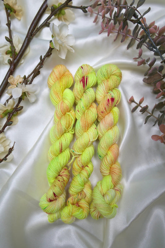 custom variegated hand dyed yarn with neon yellow and pastel peach with cherry red and green speckles on nylon superwash sock yarn