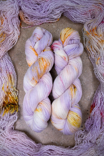 custom variegated hand dyed yarn with pastel lilac and soft purple with gold, orange and cherry red speckles on superwash merino yarn fingering weight