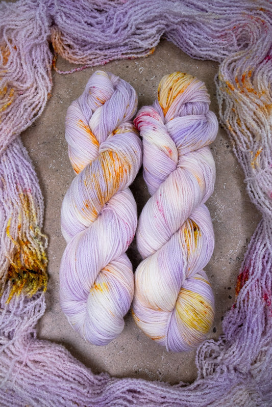 custom variegated hand dyed yarn with pastel lilac and soft purple with gold, orange and cherry red speckles on superwash merino yarn fingering weight