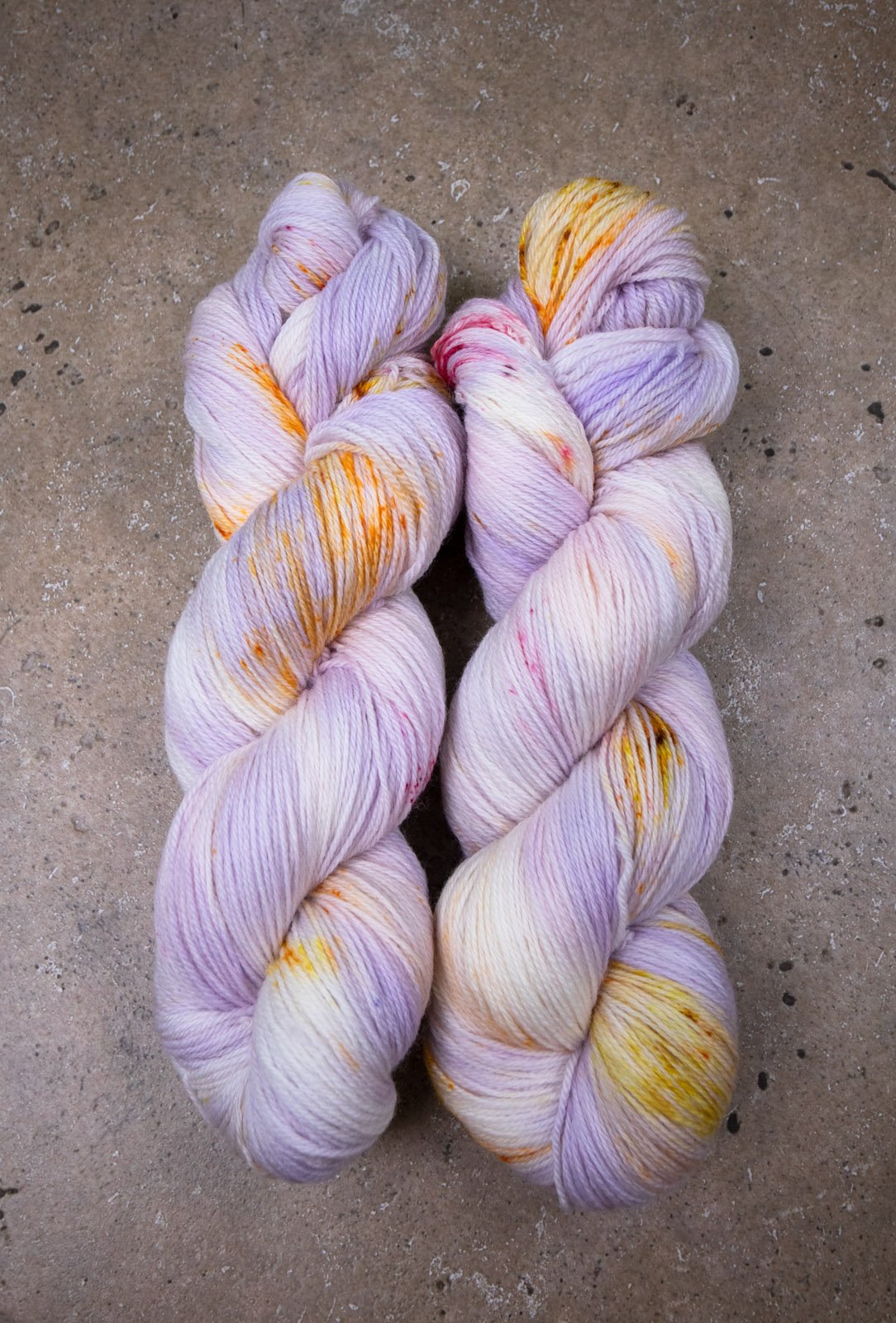 custom variegated hand dyed yarn with pastel lilac and soft purple with gold, orange and cherry red speckles on superwash merino yarn fingering weight