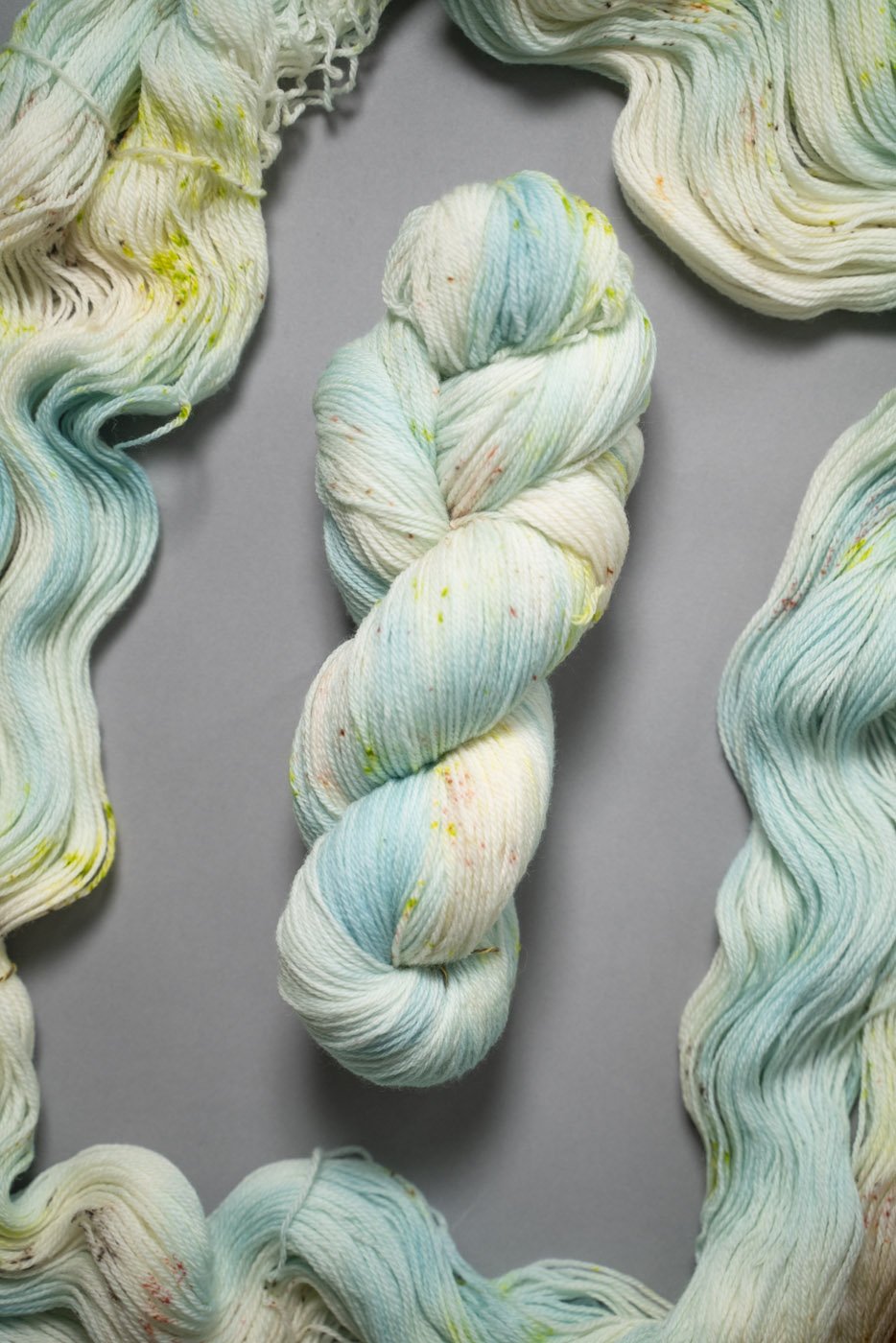 custom aqua, sky blue, teal variegated hand dyed yarn with neon green and salmon pink speckles on superwash merino fingering weight