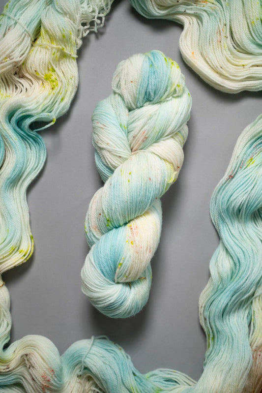 custom aqua, sky blue, teal variegated hand dyed yarn with neon green and salmon pink speckles on superwash merino fingering weight