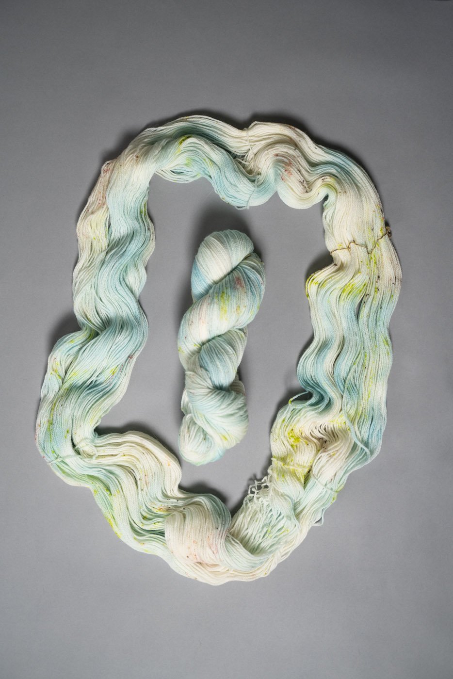 custom aqua, sky blue, teal variegated hand dyed yarn with neon green and salmon pink speckles on superwash merino fingering weight