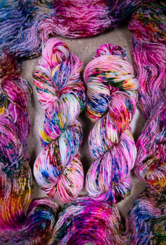 custom variegated hand dyed yarn with blue, neon pink, lichen, magenta, cherry red and yellow speckles on superwash merino worsted weight 